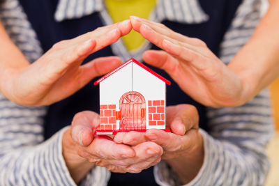 elder hands protecting a small toy house